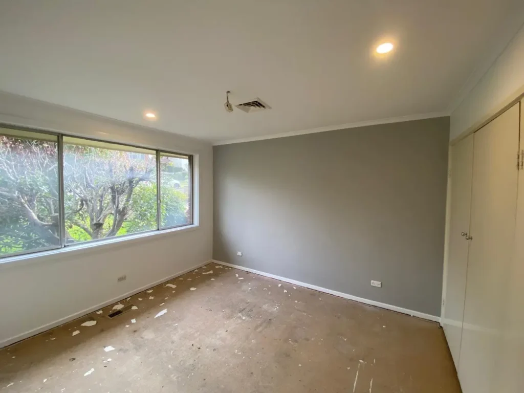 Professionally painted residential room featuring a modern grey accent wall, white ceiling with downlights, and clean white window trim.